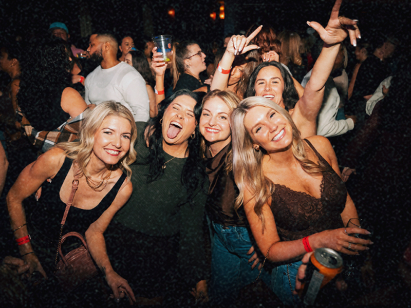 A group of women laughing and dancing close together at a Bump & Grind night party