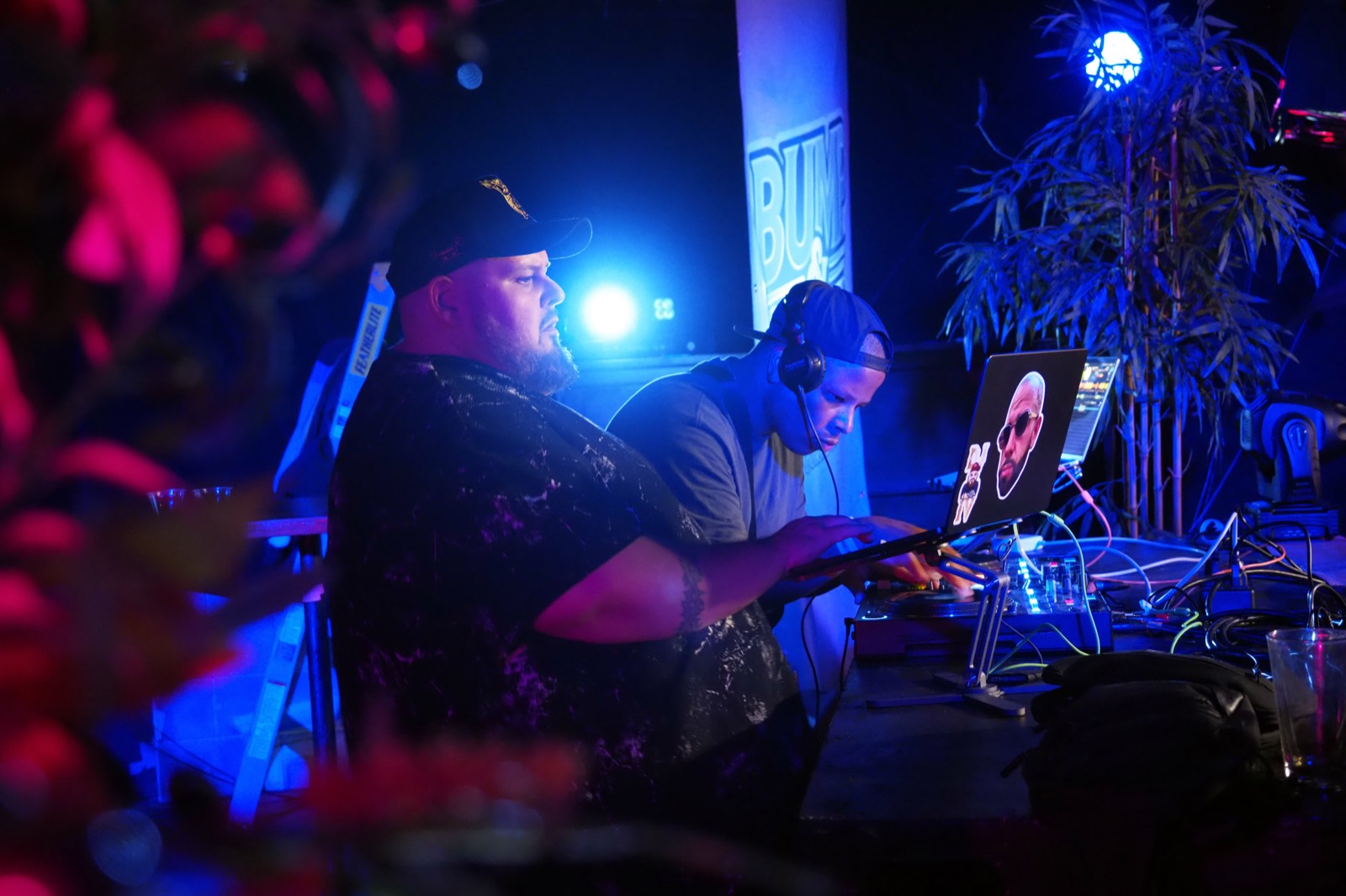 Two DJs behind the decks under blue stage lights in front of the Bump & Grind banner