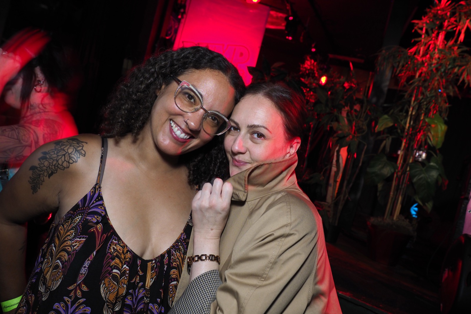 Two friends hugging and smiling under red lighting at a Bump & Grind night