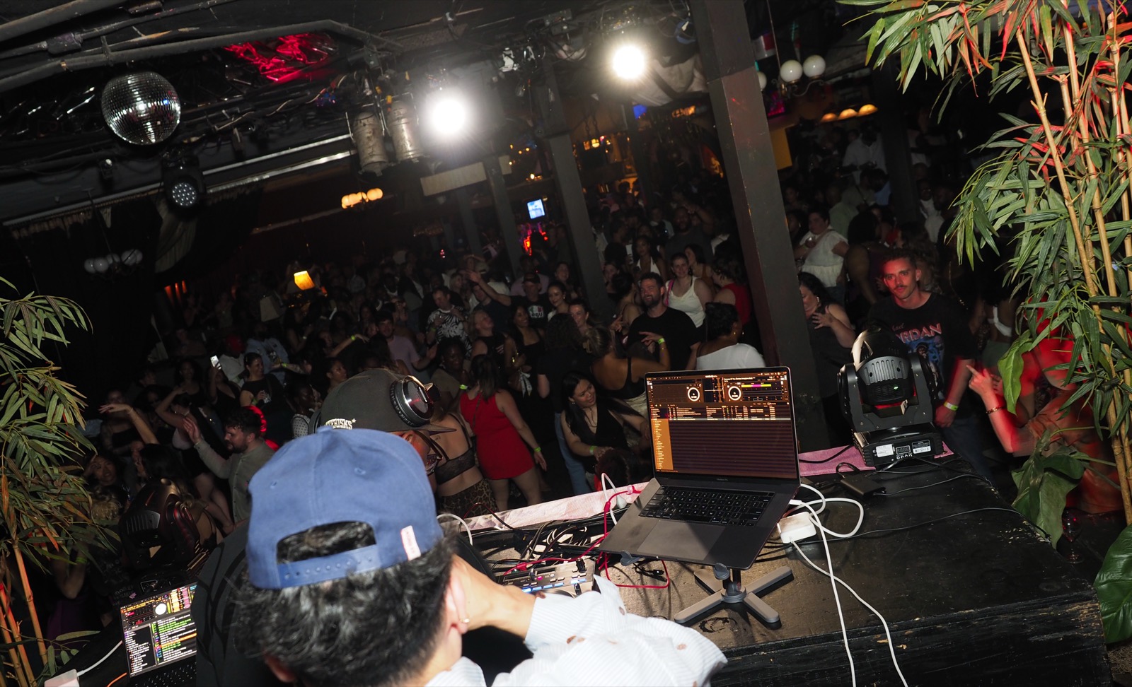 View over the DJ's shoulder of a packed crowd under the club lights
