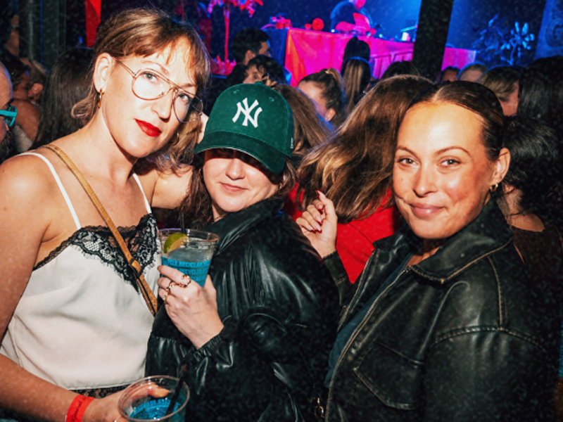 Three friends posing near the DJ booth, lit in pink and blue